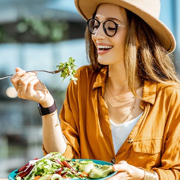 Woman with sunglasses and straw hat eating a salad