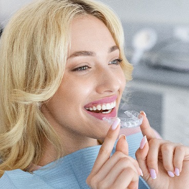 Blonde woman in dental chair about to put on a clear aligner