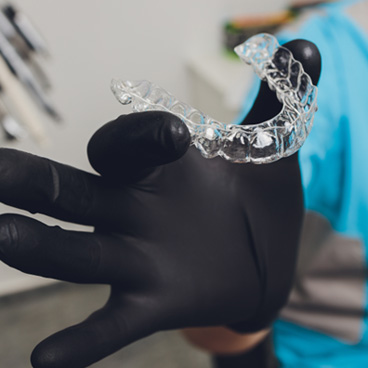 Dentist with black glove holding clear aligner