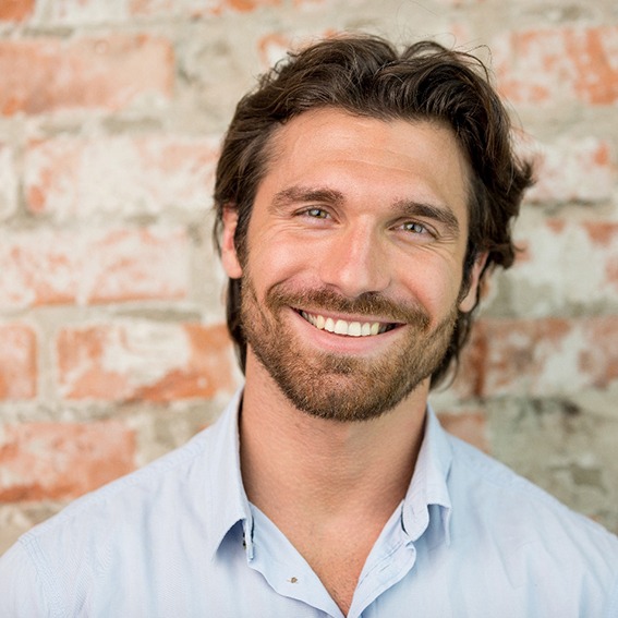 Man in collared shirt smiling in front of a brick wall