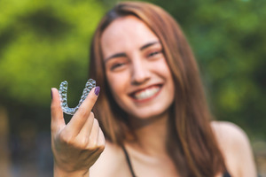 Woman smiling outside holding Invisalign aligner