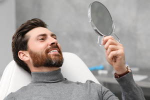Man sitting back in dental chair checking smile in mirror